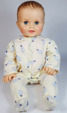 a baby doll sitting on top of a white floor next to a gray background with blue eyes