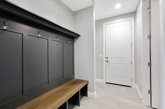 a wooden bench sitting next to a white door in a room with gray walls and flooring