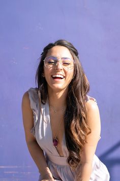 a woman sitting on the ground with her eyes closed wearing glasses and smiling at someone