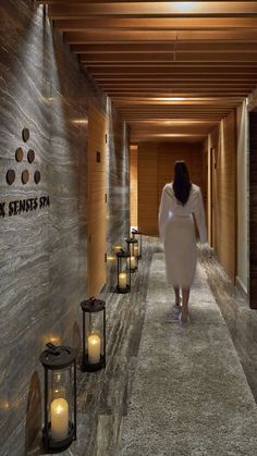 a woman walking down a long hallway with lanterns on either side of the walkway and candles in front of her