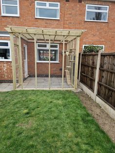 a small backyard with a chicken run in the middle and a brick building behind it