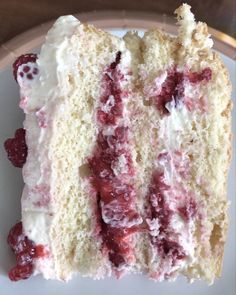 a piece of cake with white frosting and raspberries on top is sitting on a plate