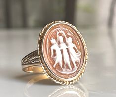 "Cameo ring; beautiful \"Three Graces\" hand carved genuine Italian cameo set in solid 10K yellow gold. The shell cameo is bezel set and measures 20 mm x 15 mm. In Greek mythology, the Three Graces were more commonly known as the Charites, although today, the Roman name, the Graces, is more often used. The Charites, or Graces, were three sisters, minor goddesses, and daughters of Zeus and the Oceanid Eurynome. Hesiod, in the Theogony, named the Three Graces as, Aglaea, Thalia and Euphrosyne. The Gold Cameo Rings For Anniversary, Cameo Rings As Gift In Fine Jewelry Style, Yellow Gold Cameo Rings For Gifts, Intaglio Ring For Wedding, Wedding Intaglio Jewelry Ring, Intaglio Wedding Ring Jewelry, Intaglio Wedding Ring, White Gold Intaglio Rings For Wedding, Cameo Fine Jewelry Rings