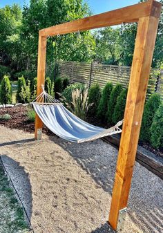 a hammock hanging from a wooden frame in a backyard area with gravel and trees