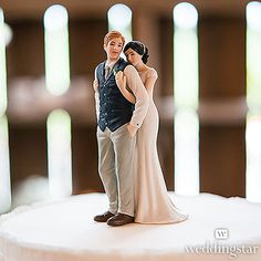 a bride and groom figurine standing on top of a white frosted cake