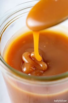 caramel sauce being drizzled onto a spoon in a glass jar with liquid