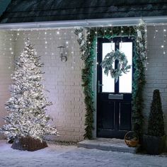 a white christmas tree sitting in front of a house with lights on it's windows