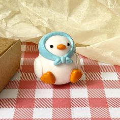 a penguin figurine sitting on top of a checkered table cloth next to a box