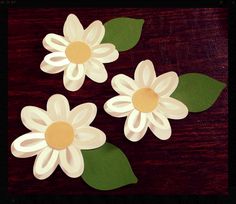 three paper flowers with green leaves on a wooden table, ready to be cut out