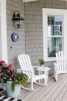 two white chairs sitting on top of a wooden porch next to a potted plant