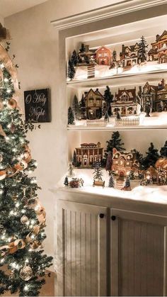 a christmas tree is in front of a shelf filled with miniature houses and other decorations