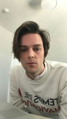 a man with long hair sitting at a table in front of a laptop computer and looking into the camera