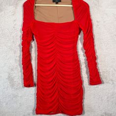 a red dress with long sleeves and pleating on the shoulders is hanging on a hanger