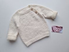 a white knitted sweater next to a small tag on a white surface with an image of a woman's face