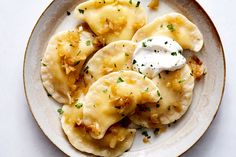 a white plate topped with dumplings covered in cheese and sour cream on top of a table