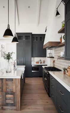 a large kitchen with black cabinets and white counter tops, wooden flooring and hanging lights