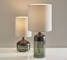 two table lamps sitting next to each other on top of a white counter with a lamp in the middle