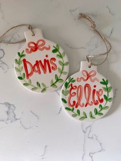 two ceramic ornaments with names on them sitting on a marble counter top, one is red and the other is green