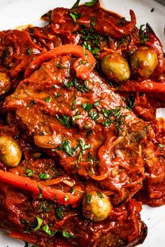 a white plate topped with meat covered in sauce and vegetables