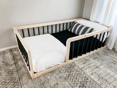 a black and white crib with two pillows on the bottom, next to a window