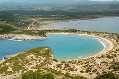 an aerial view of the beach and ocean near some hills with trees on them in front of blue water