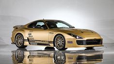 the gold sports car is parked in front of a white wall and reflective flooring