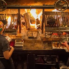 two people cooking food in front of a fire