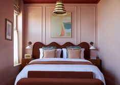 a bedroom with pink walls and white bedding has a painting on the wall above it