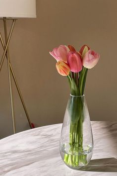 pink and yellow tulips in a clear vase on a marble table with a lamp