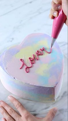 someone is decorating a heart shaped cake with the word love spelled in pink on it