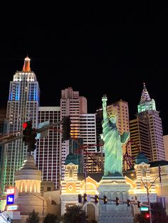 the statue of liberty is lit up at night in front of buildings and traffic lights