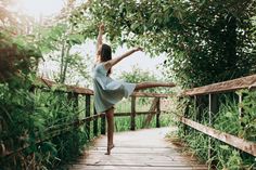 a woman in a white dress is dancing on a wooden bridge surrounded by greenery