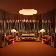 a living room with two chairs, speakers and a couch in front of a curtained wall