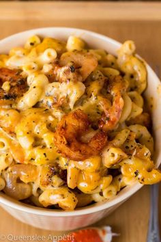 a white bowl filled with macaroni and cheese next to a fork on a wooden table