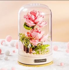 pink flowers are in a glass dome on a white surface with tiny balls around it