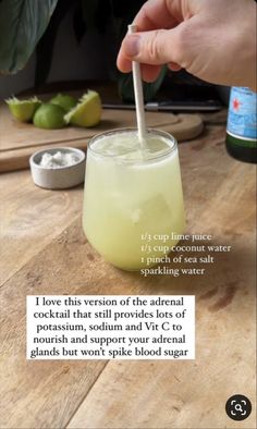 a person is holding a straw in a glass with limes on the table next to it