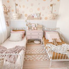 two twin beds in a small room with floral wallpaper and pink accents on the walls