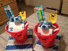 two red buckets with toothbrushes and stuffed animals in them on a bed