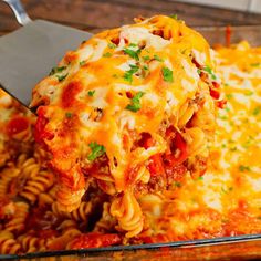 a spatula scooping some pasta out of a casserole dish with meat and cheese