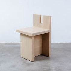 a small wooden chair sitting on top of a cement floor next to a white wall