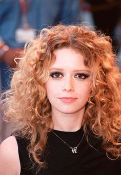 a close up of a person with long curly hair wearing a black shirt and necklace