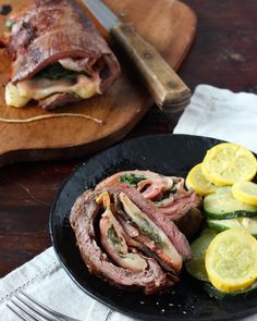 a black plate topped with meat and sliced up zucchini next to a cutting board