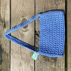 a blue crocheted purse sitting on top of a wooden table next to a tag