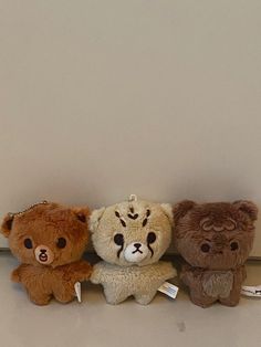 three teddy bears sitting next to each other on a shelf in front of a wall