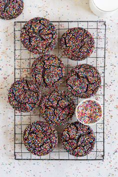 sprinkle covered donuts on a cooling rack next to a cup of coffee