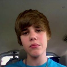 a young man wearing a blue shirt in the back seat of a car looking at the camera