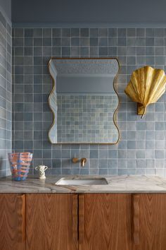 a bathroom with blue tiled walls and wooden cabinetry, gold mirror above the sink