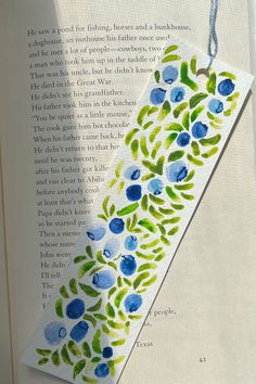 an open book with blue flowers and green leaves on the cover, hanging from a string