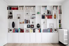 a white book shelf filled with lots of books next to a radiator and heater