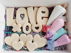 the word love spelled out with cookies and other items in a white box on top of sprinkles